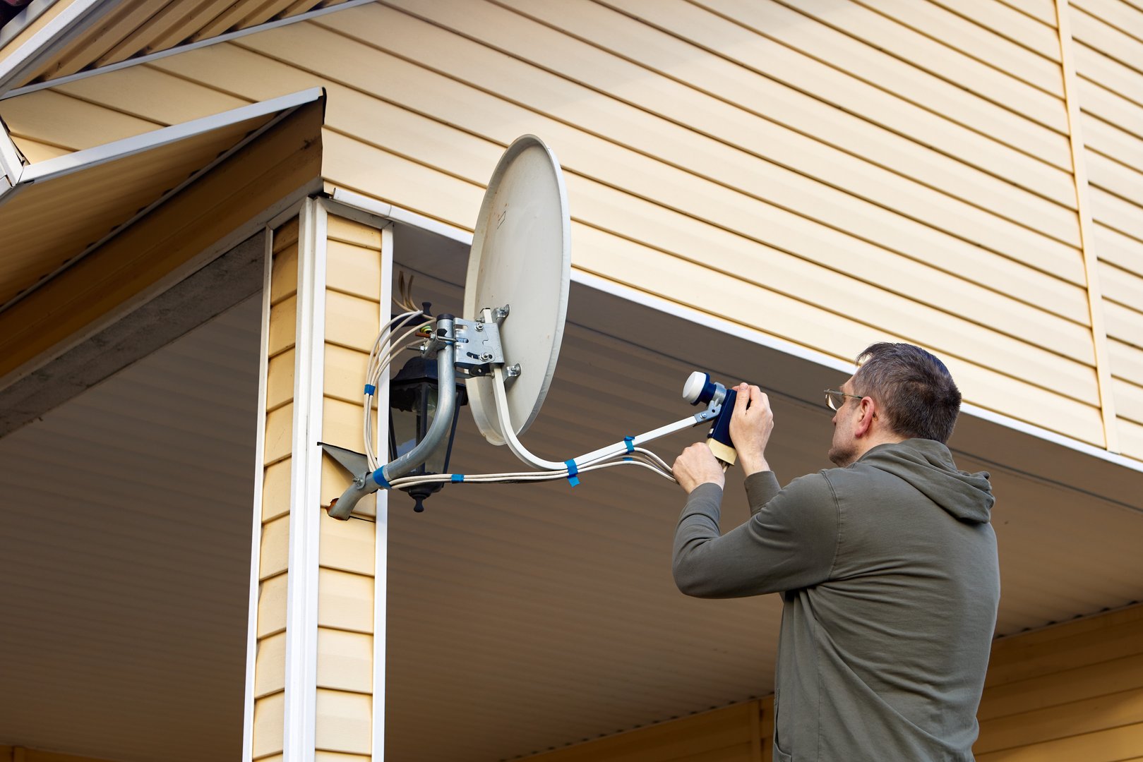 Repairer is repairing satellite TV dish in countryside at summer day.