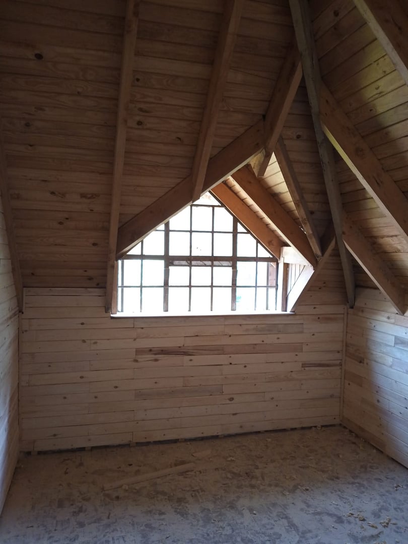 Wooden interior with sloped ceiling, triangular window, and exposed beams.
