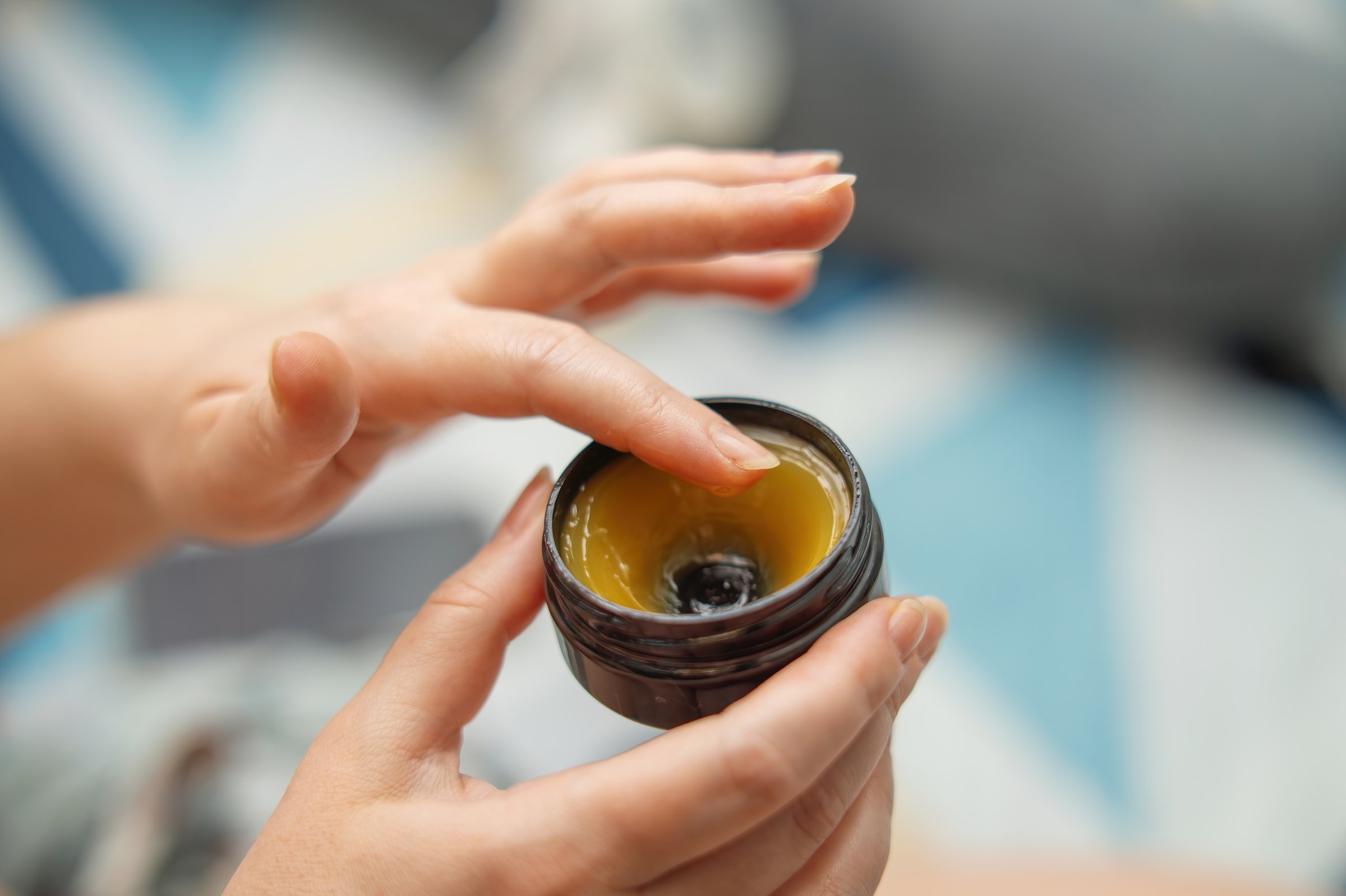 women hands applying lanolin cream from jar, designed for soothing and healing breasts after breastfeeding, showcasing self-care and maternal wellness