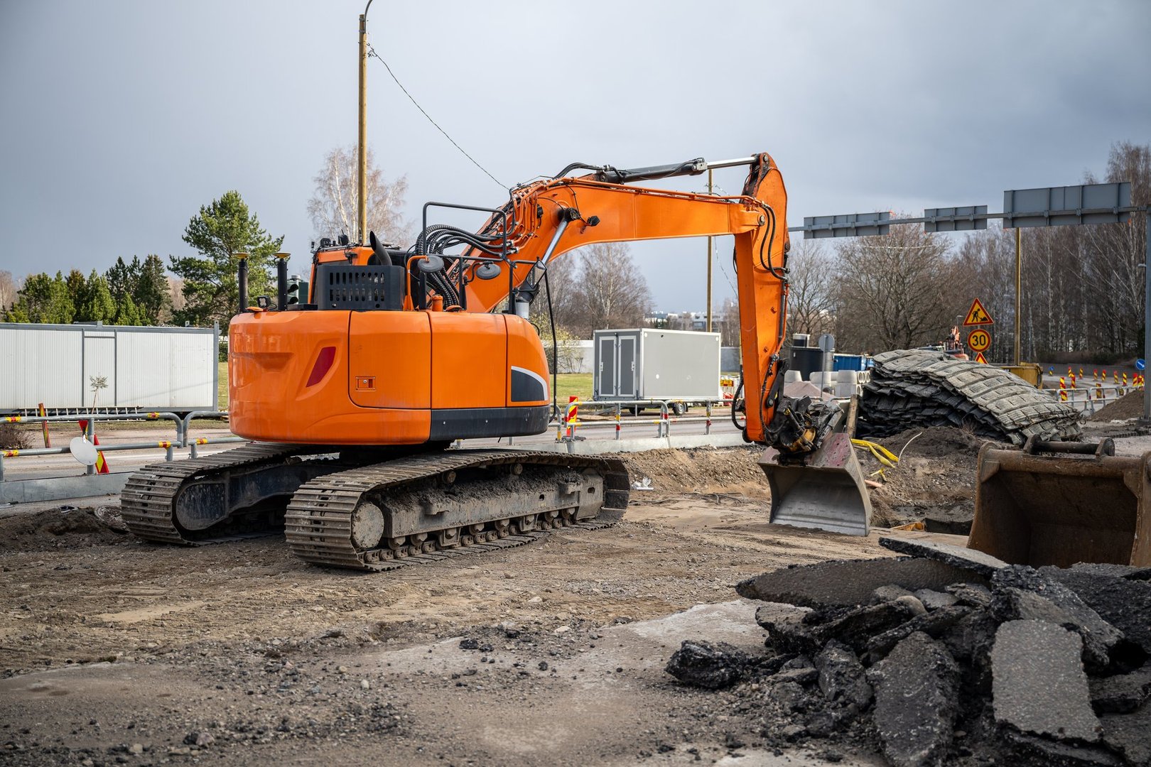 broken asphalt and orange excavator at road construction site