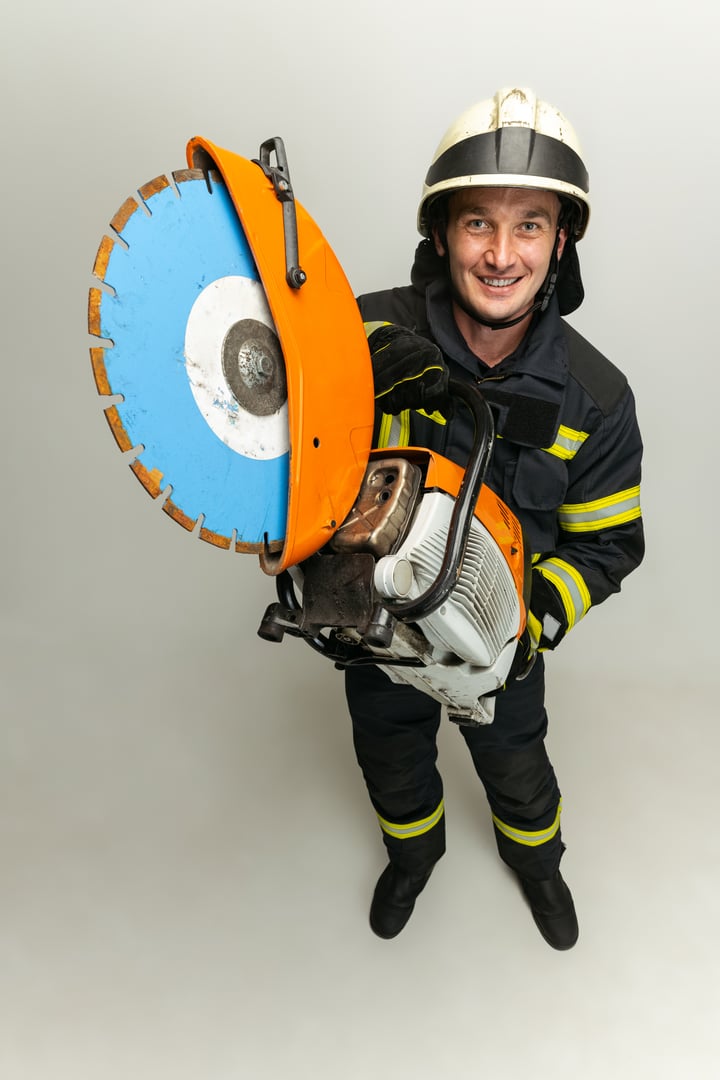 Studio portrait of male firefighter dressed in uniform with electric saw in his hands over white background. Concept of different professions and unusual people.