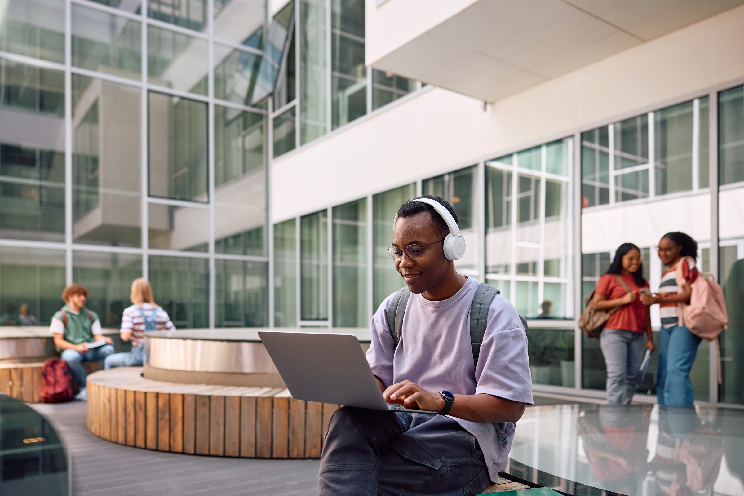 Happy African American university student with headphones using laptop at campus. Copy space.