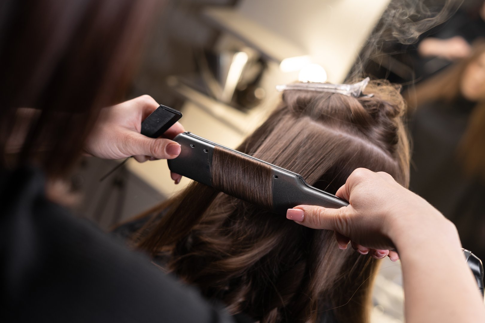 close-up of the hands of the master in the spa salon straighten the hair with an iron in the spa salon. keratin hair restoration and protein hair