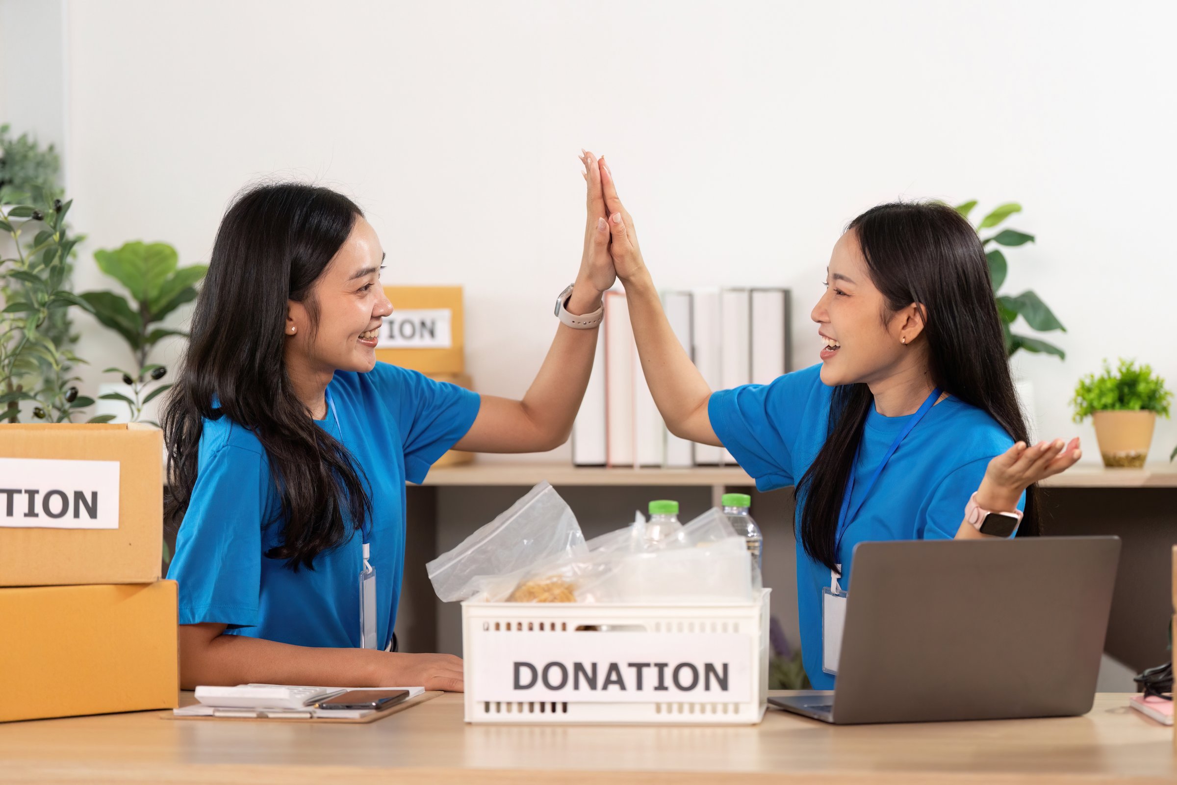 Two volunteers share a joyful moment while organizing donations, showcasing teamwork and community spirit.