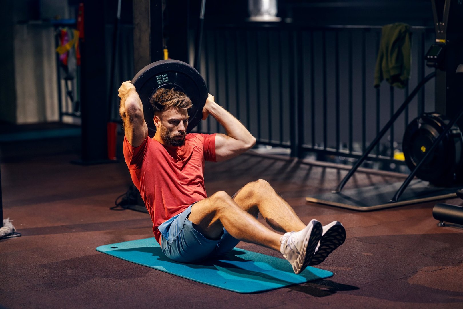 Powerful sportsman doing strength workouts at gym with weight plate.
