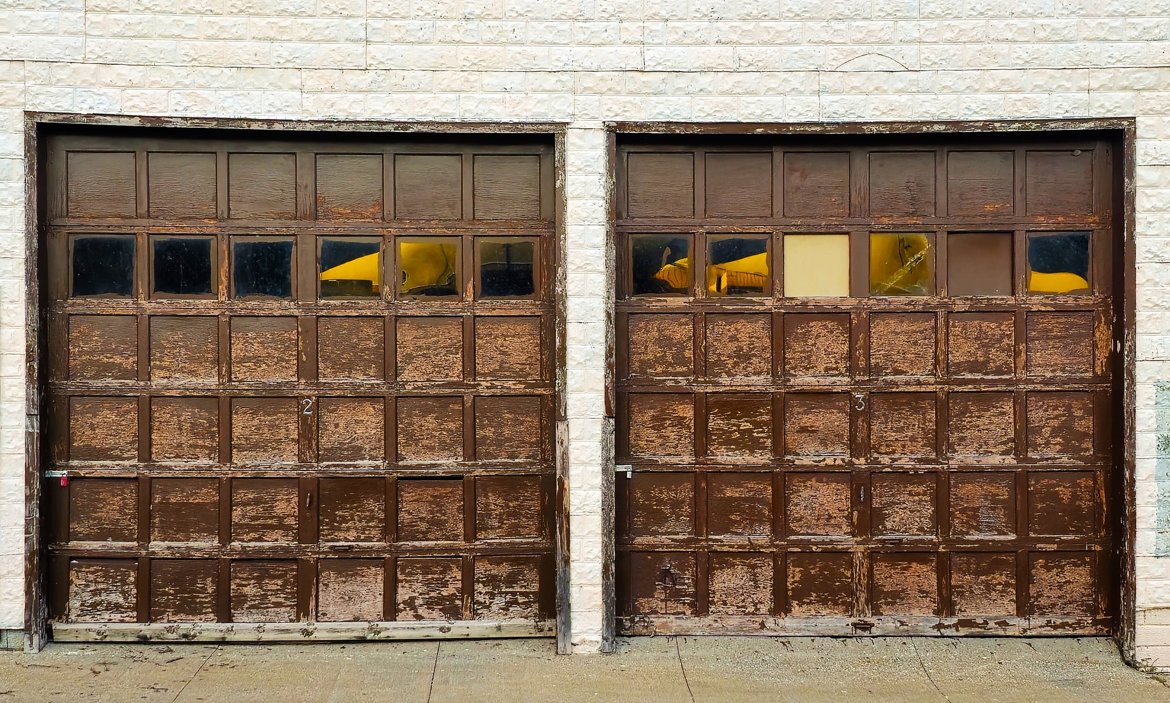 pair of rustic old brown garage doors on white brick building background