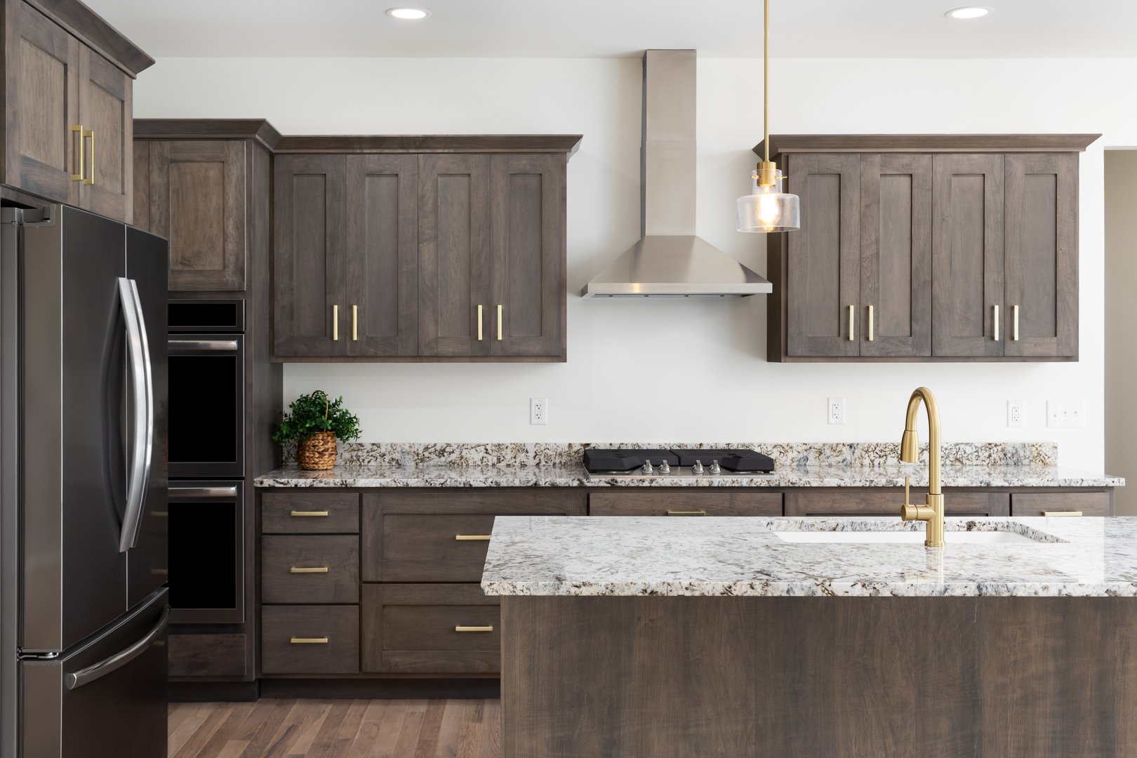 A kitchen detail with a gold faucet on a granite countertop,dark wood cabinets, stainless steel appliances, and gold pendant lights hanging above the island.