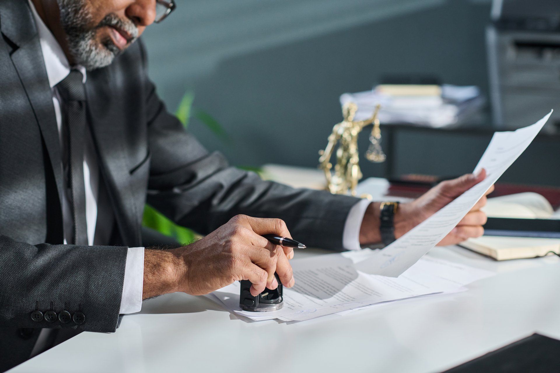 Cropped shot of mature male adviser or director of company putting stamp on documents while sitting by workplace in office