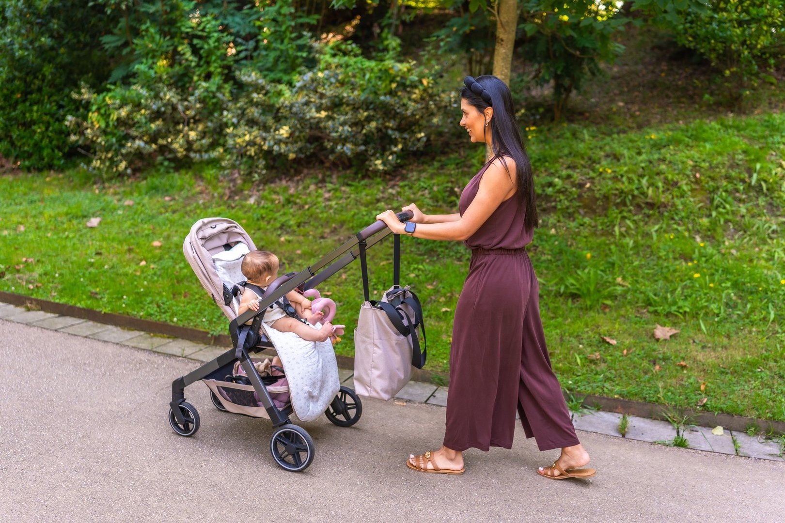 Latin mother pushing a stroller with her baby girl, enjoying a leisurely walk in the park on a bright, sunny summer day