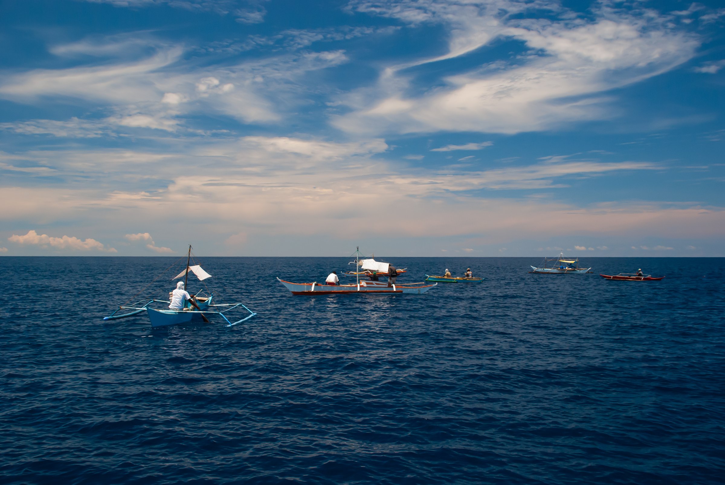 Fleet of small boats fishing for tuna in the middle of the sea under a beautiful cloudy and blue sky