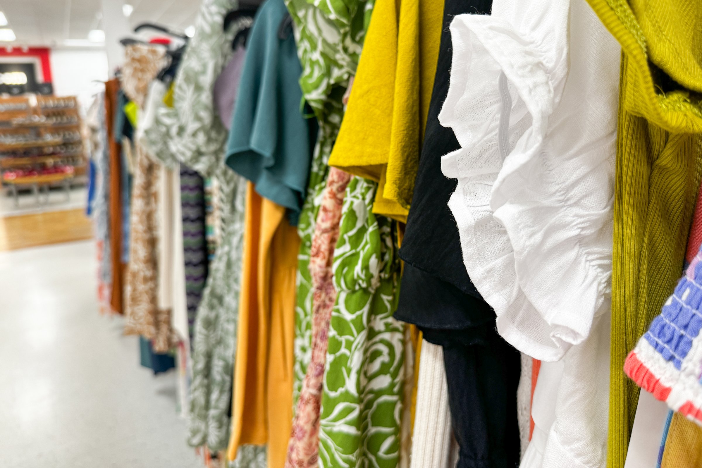 A row of colorful clothes is neatly displayed on hangers in a retail clothing store aisle