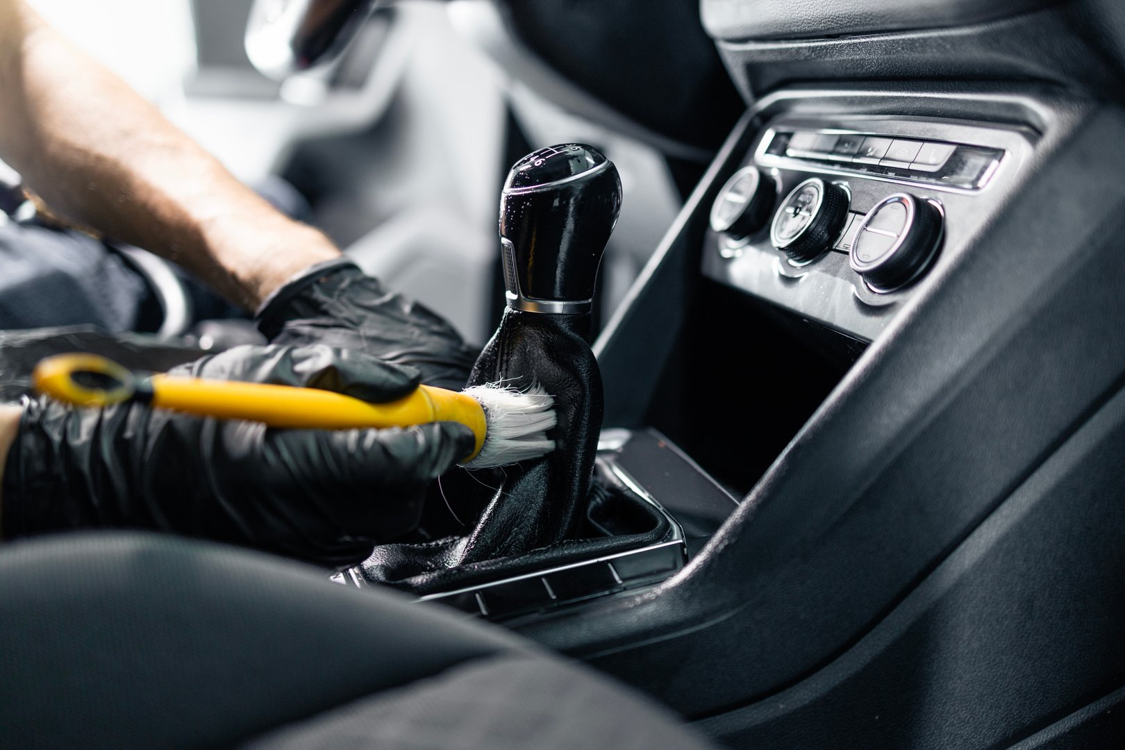 Professional cleaner using soft brush to clean dust inside car interior.