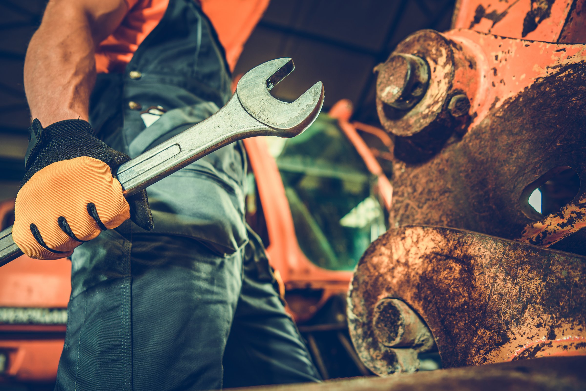 A muscular Caucasian mechanic holding a large iron wrench in his hand