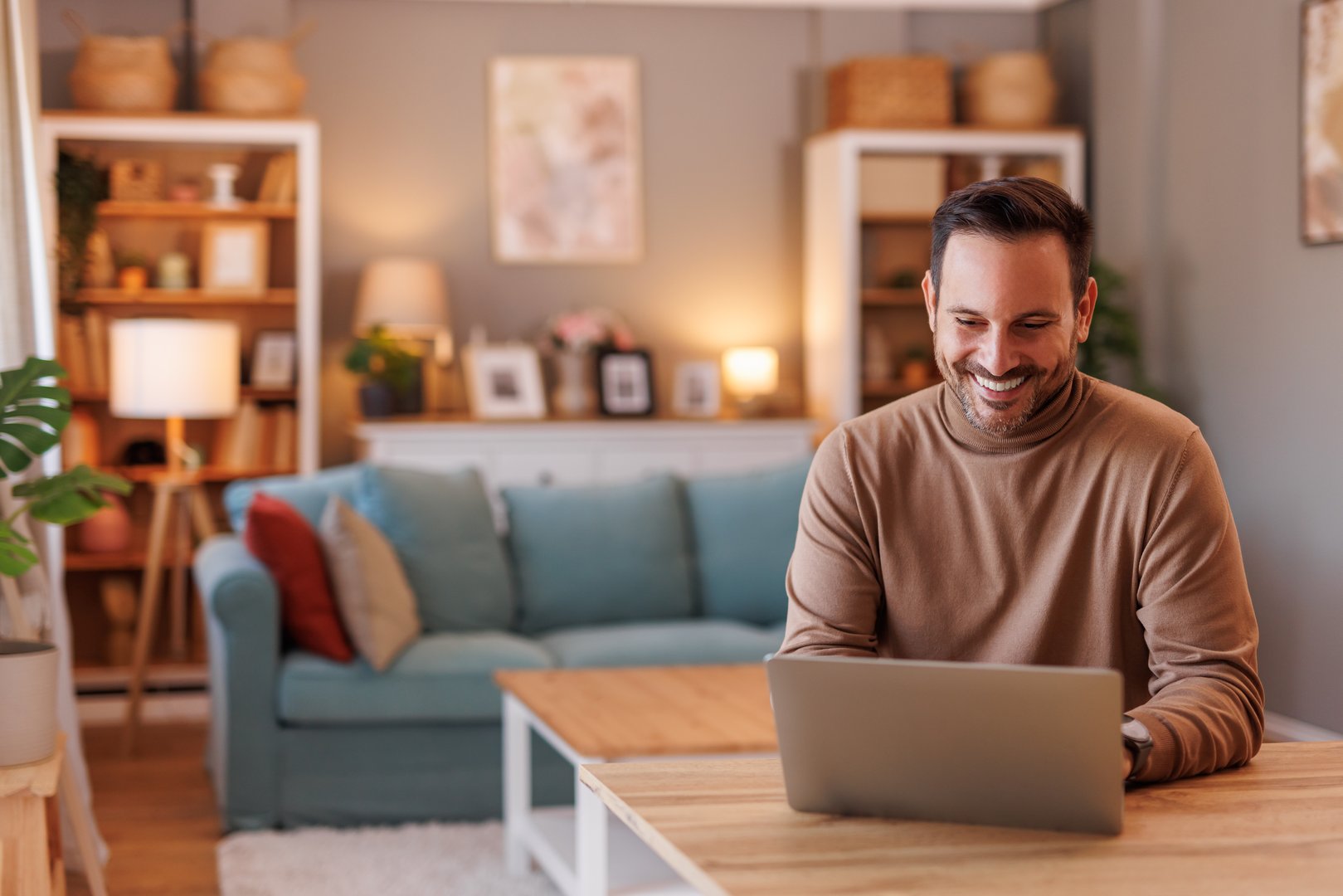 Portrait of successful male freelancer working online on project over laptop at desk in home office