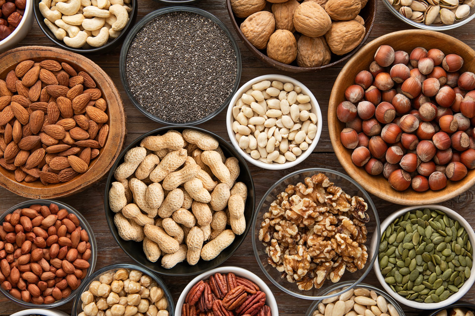 Peanut,hazelnut,walnut,almonds,pistachio,sunflower,pumpkin,chia,pecan and cashew mixed healthy nuts and seeds in various bowls on wooden background.
