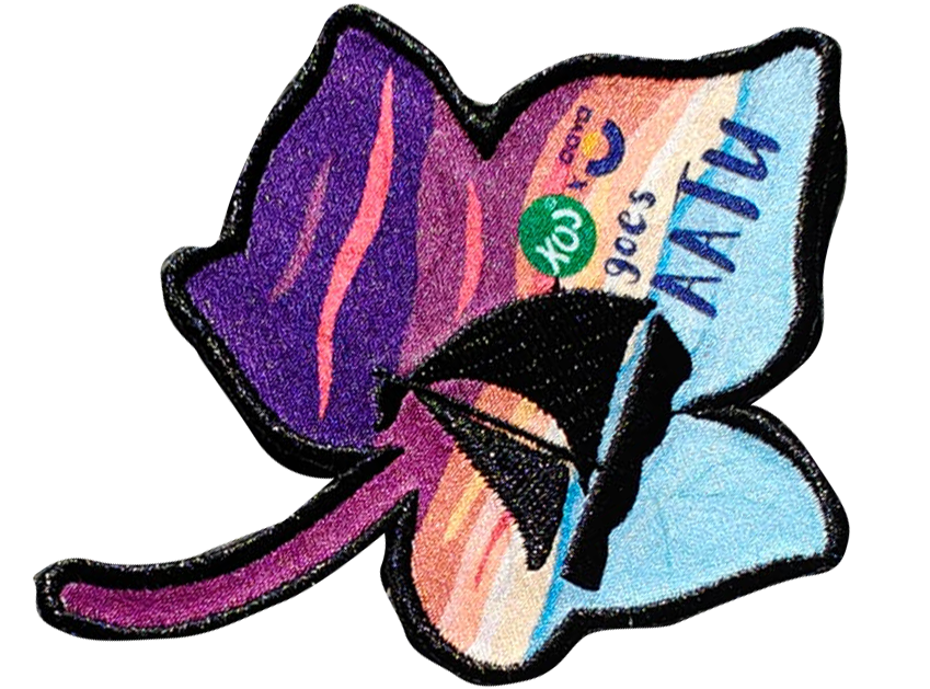 Colorful leaf-shaped patch with a sailboat design, featuring purple, orange, and blue hues and text including goes NATU.