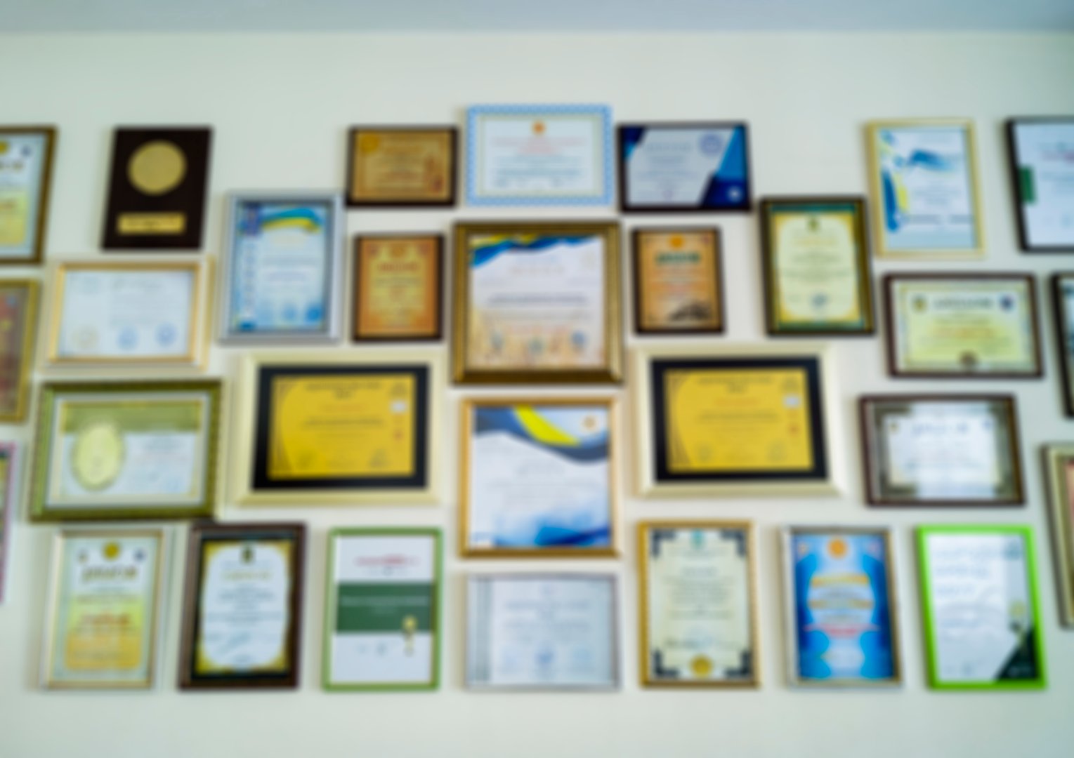 Unrecognizable certificates, diplomas and awards in frames on the wall. Abstract blurry background image.