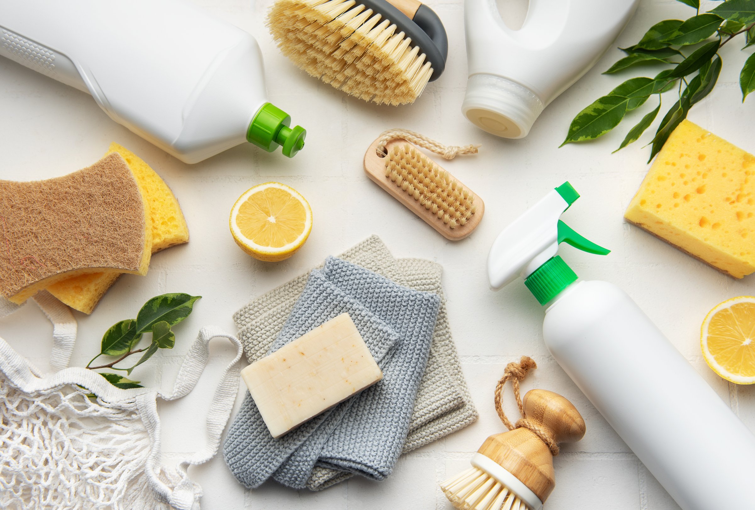 Natural cleaning products and tools arranged on white surface, promoting sustainable and eco conscious lifestyle