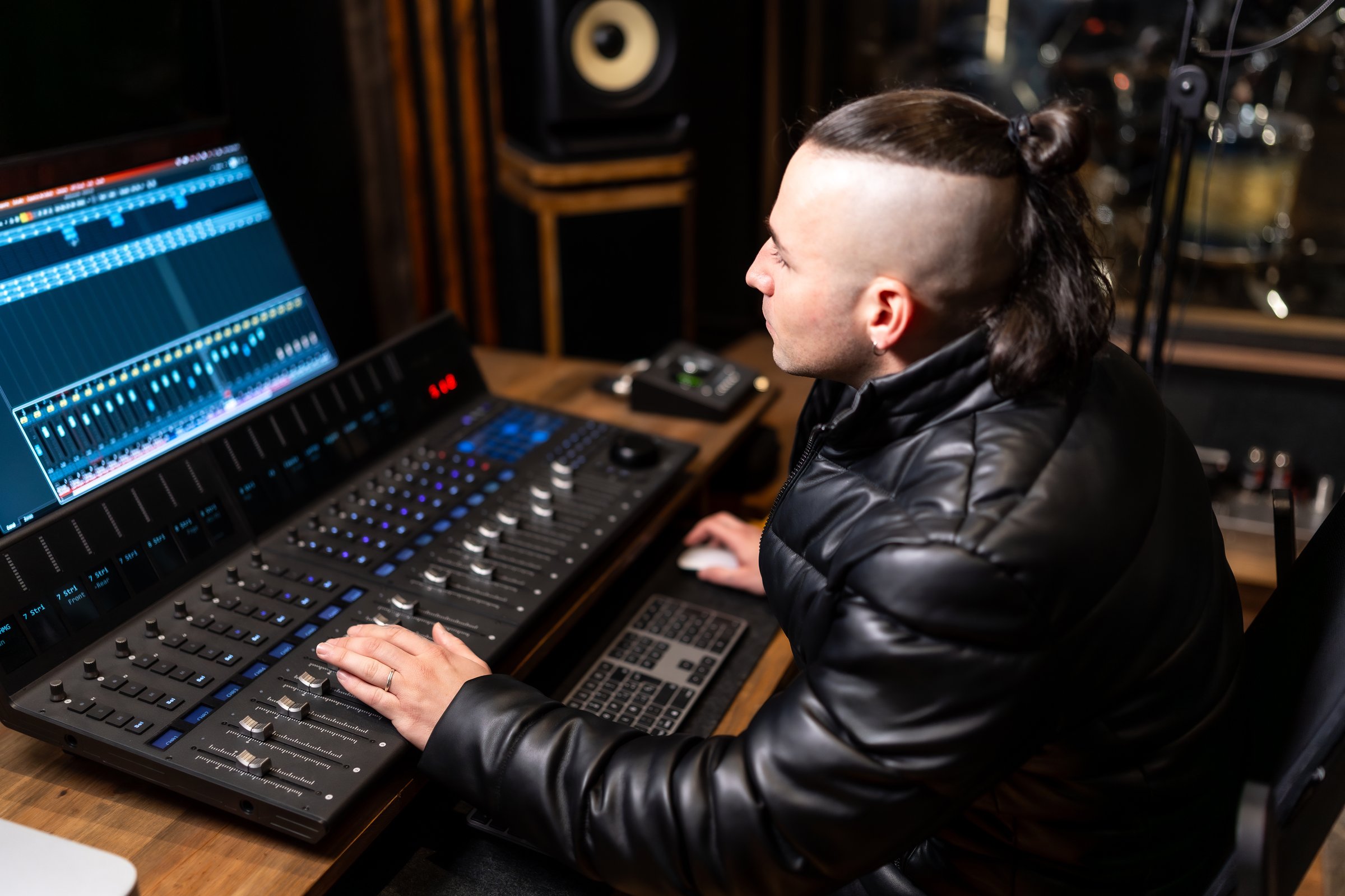 Young music producer working on a new song inside a recording studio, adjusting the levels on a mixing console