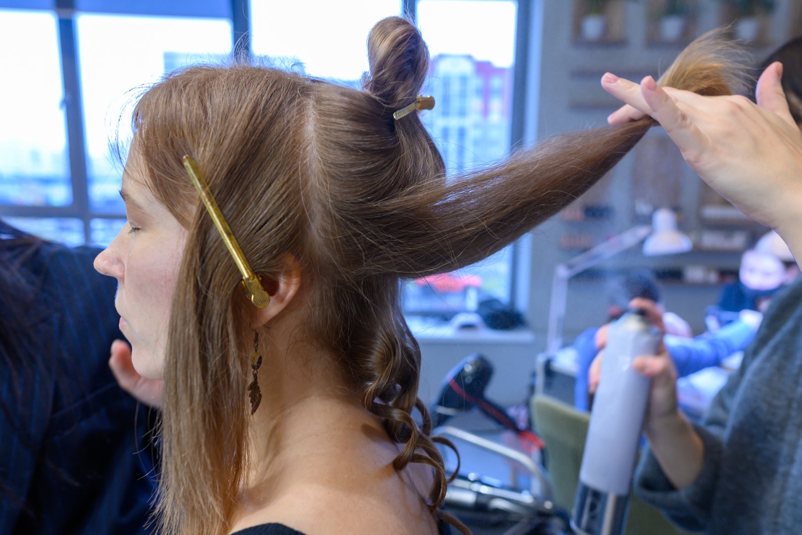 In a bright beauty salon, a stylist carefully works to create a stunning hairstyle on a client, showcasing skillful techniques and creativity.