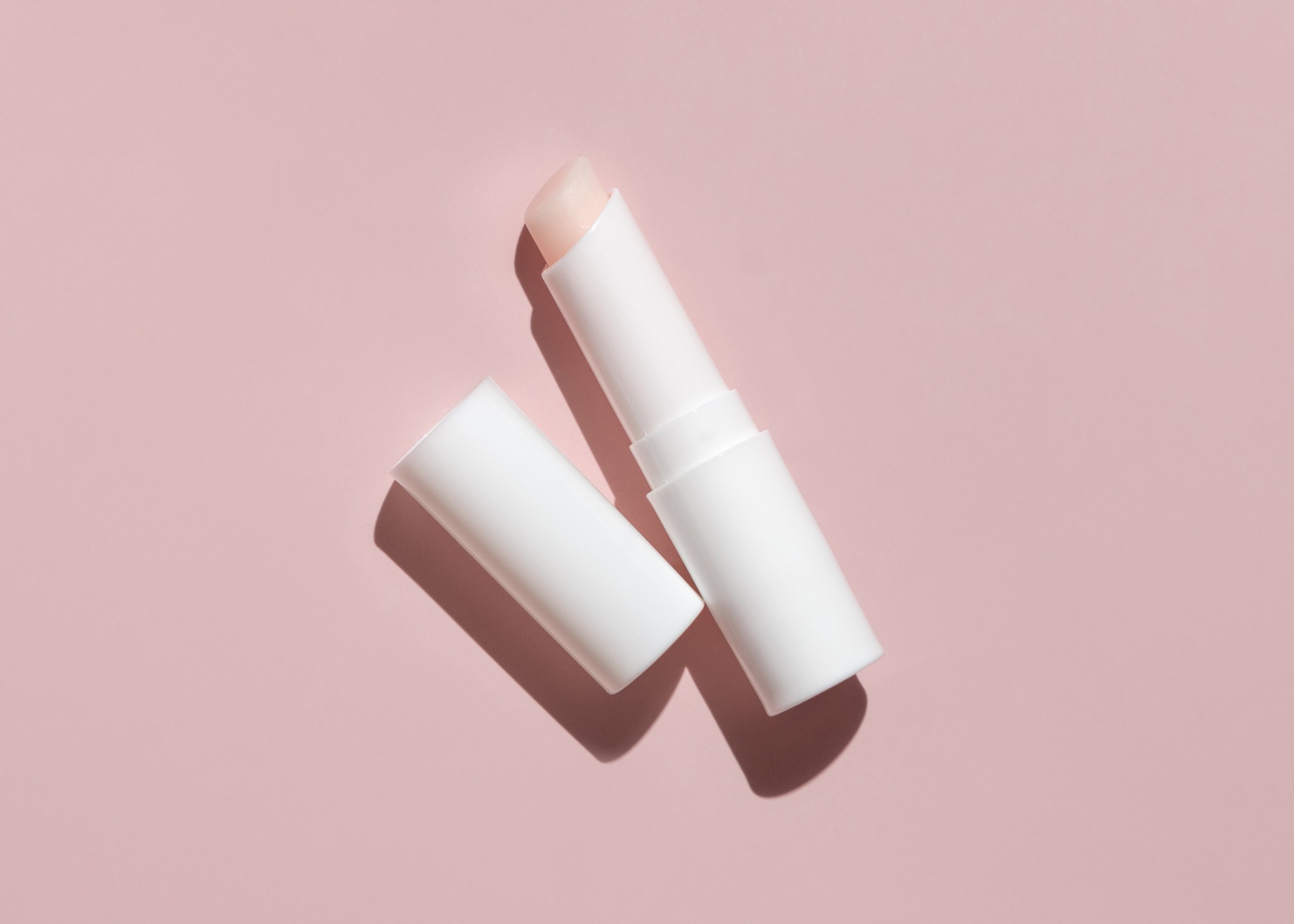 Opened white blank lip balm stick with a lid on light pink with hard shadow top view, mockup, negative space. Lipcare beauty product for mens daily personal care, minimal style aesthetic