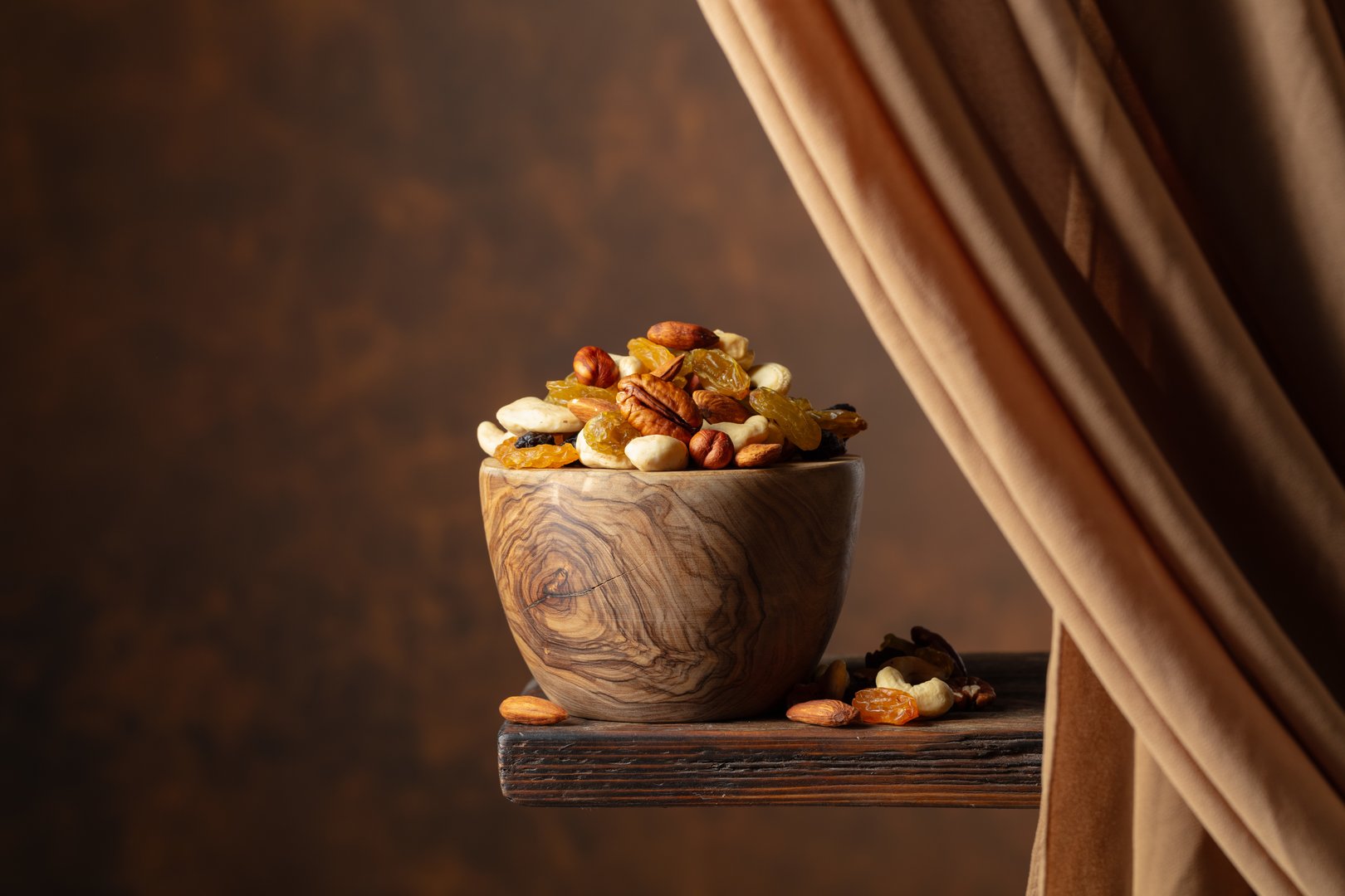The mix of various nuts and raisins in a wooden bowl on a brown background. Copy space.