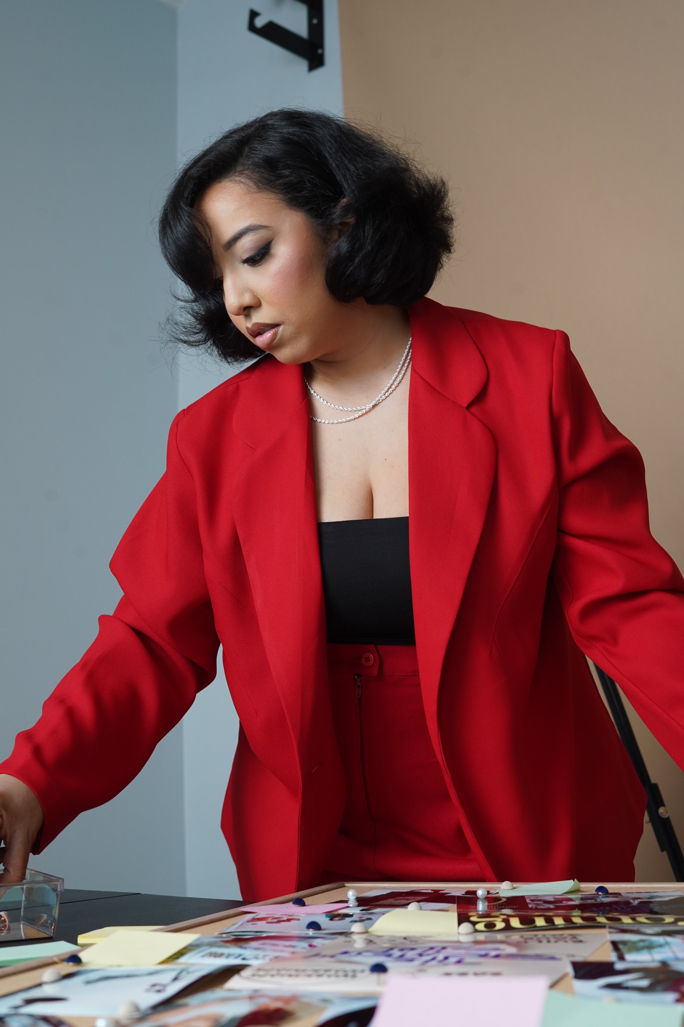 Woman in red suit arranging papers on a table, focused and engaged in work.