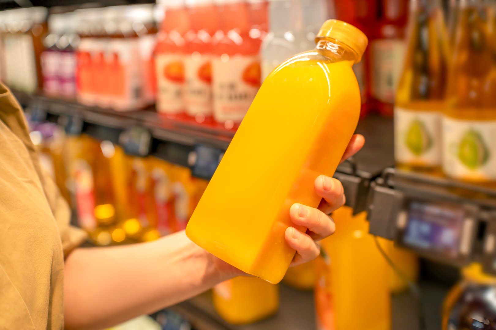 Person holding a bottle of orange juice in a supermarket