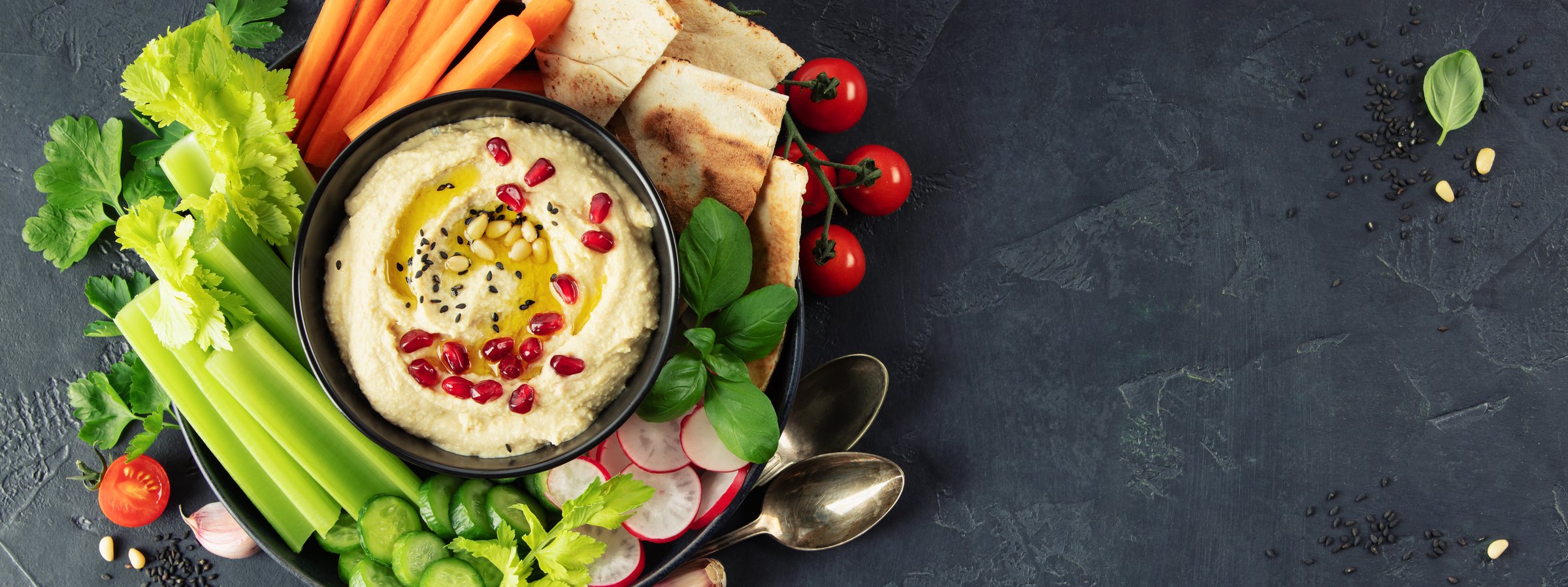 A beautifully arranged hummus platter with fresh vegetables, pita bread, pomegranate seeds, and sesame. Perfect for healthy eating concepts, menus, blogs, and banner designs.