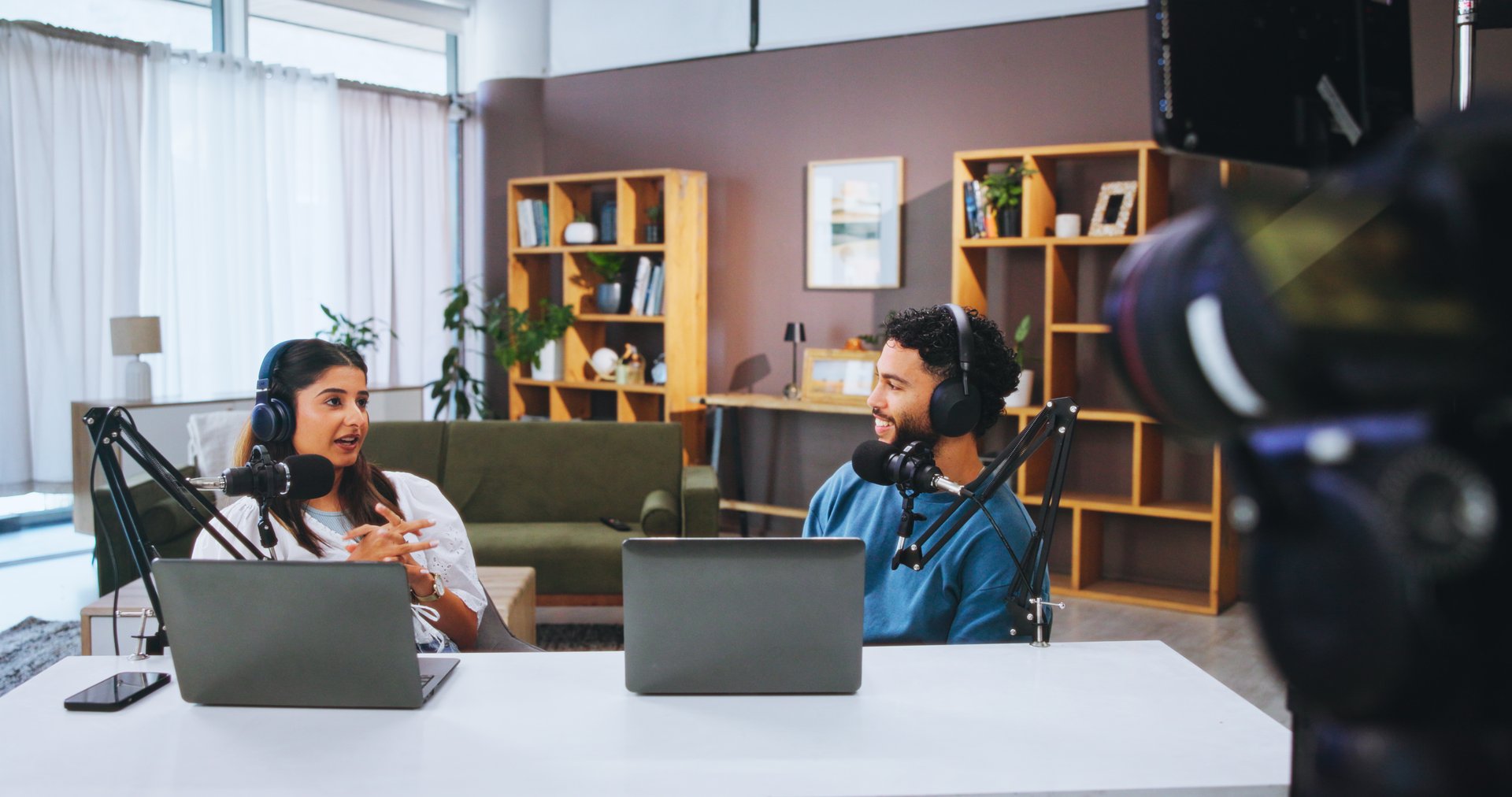 Headphones, laptop and people with mic on talk show in home studio for podcast, news broadcast or live stream. Recording, host and talking to guest for public relations, web interview or social media