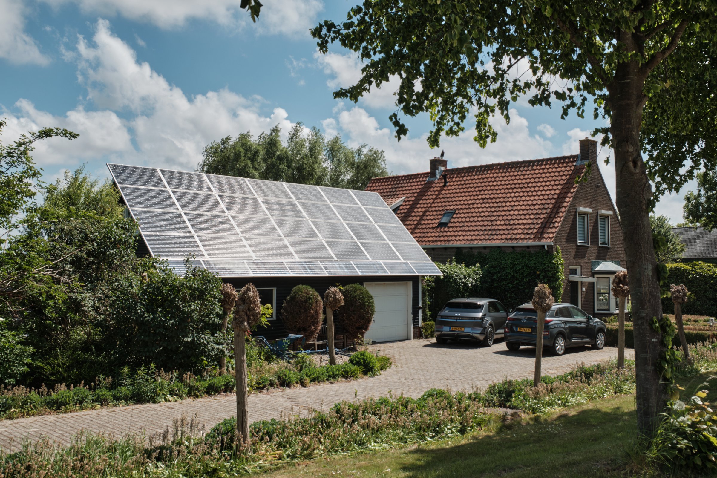 May 17, 2025 - Ovezande-Netherlands: Dutch property with garage shed full of solar panels, charging a EV, in the village of Ovezande. The solar panels even extend the roof.