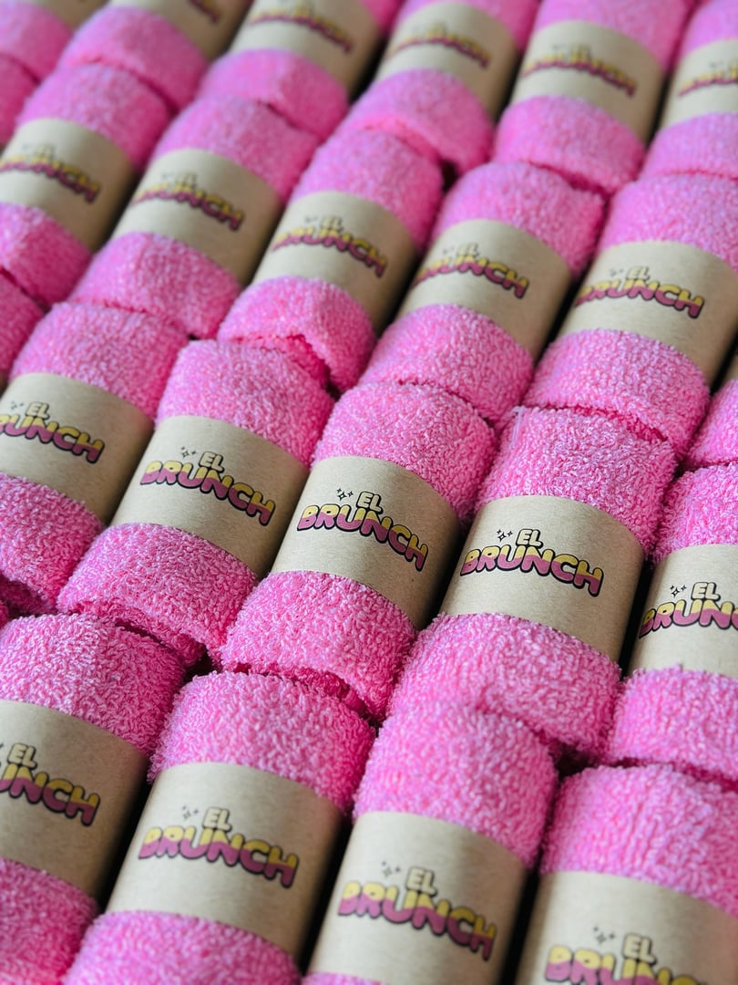 Rows of pink towels with "EL BRUNCH" labels wrapped around them, arranged neatly in a pattern.