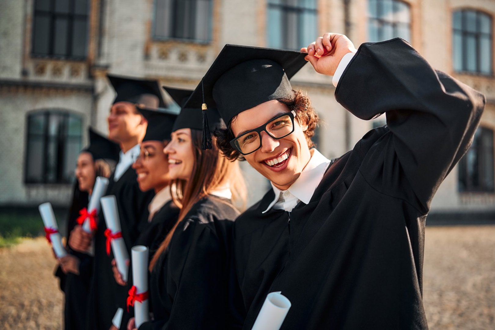 Handsome successful graduate in academic gown and cap smiling and looking at camera. Happy graduation day and celebration. Bright future.