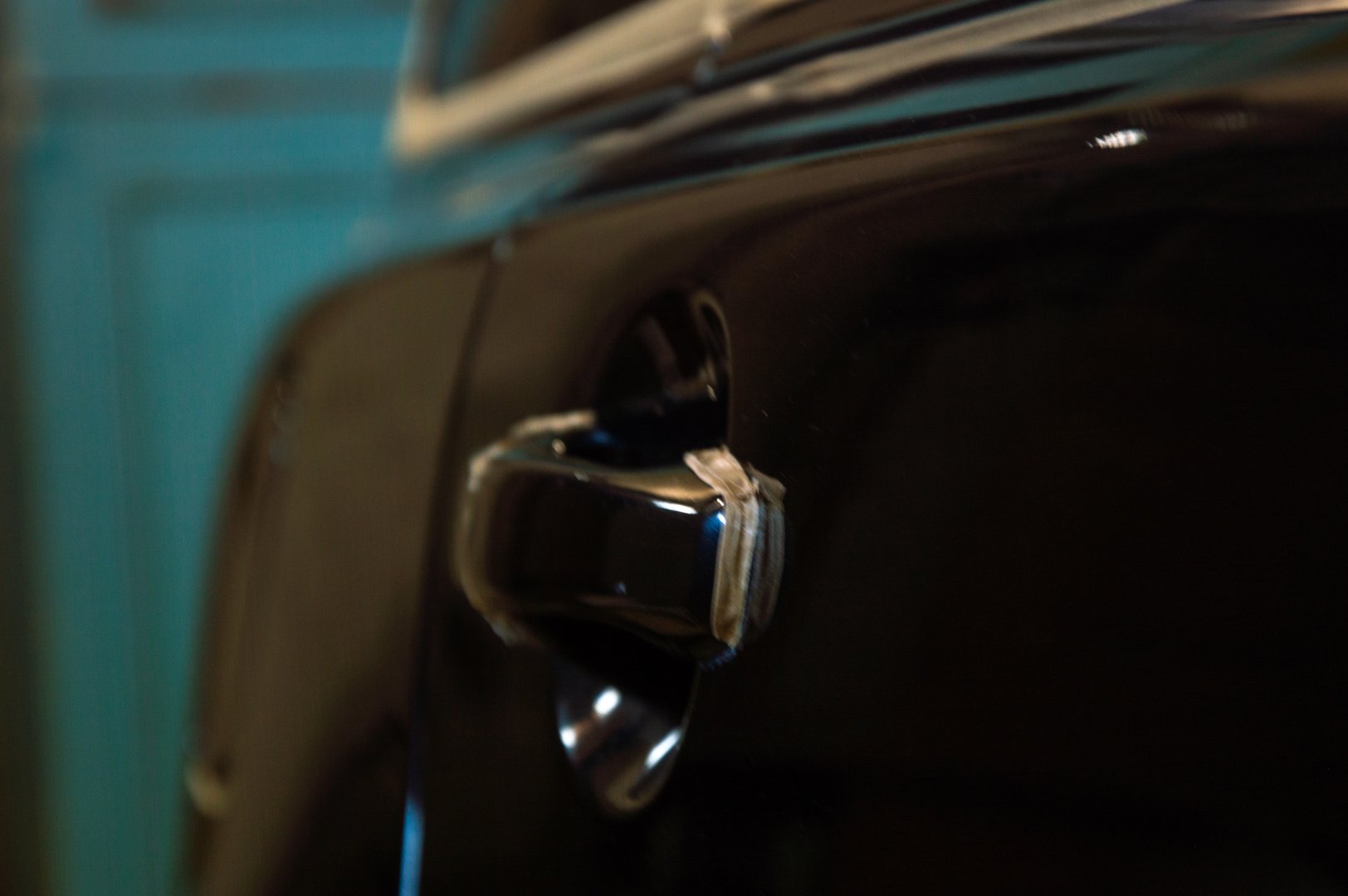 A person polishes a sleek black car, creating a shiny surface in a well-lit garage filled with tools and equipment.