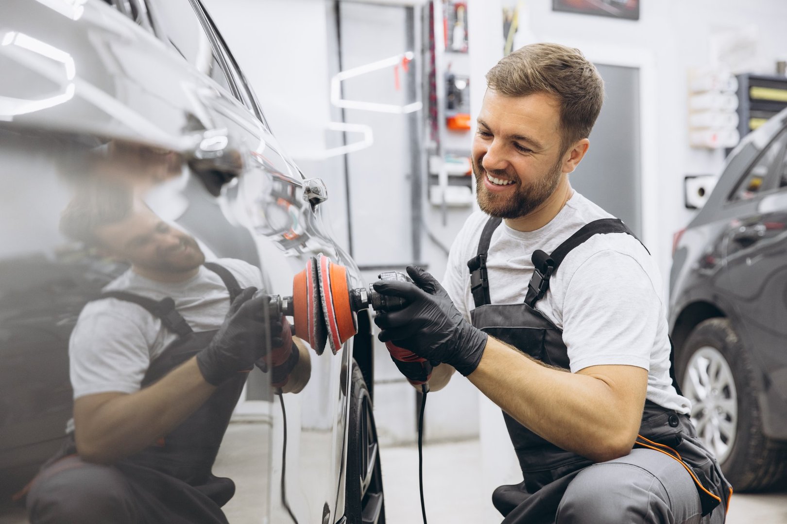 Side view of a man polishing a car using a professional auto polisher in a garage, showcasing meticulous attention to detail in car maintenance and cleaning.