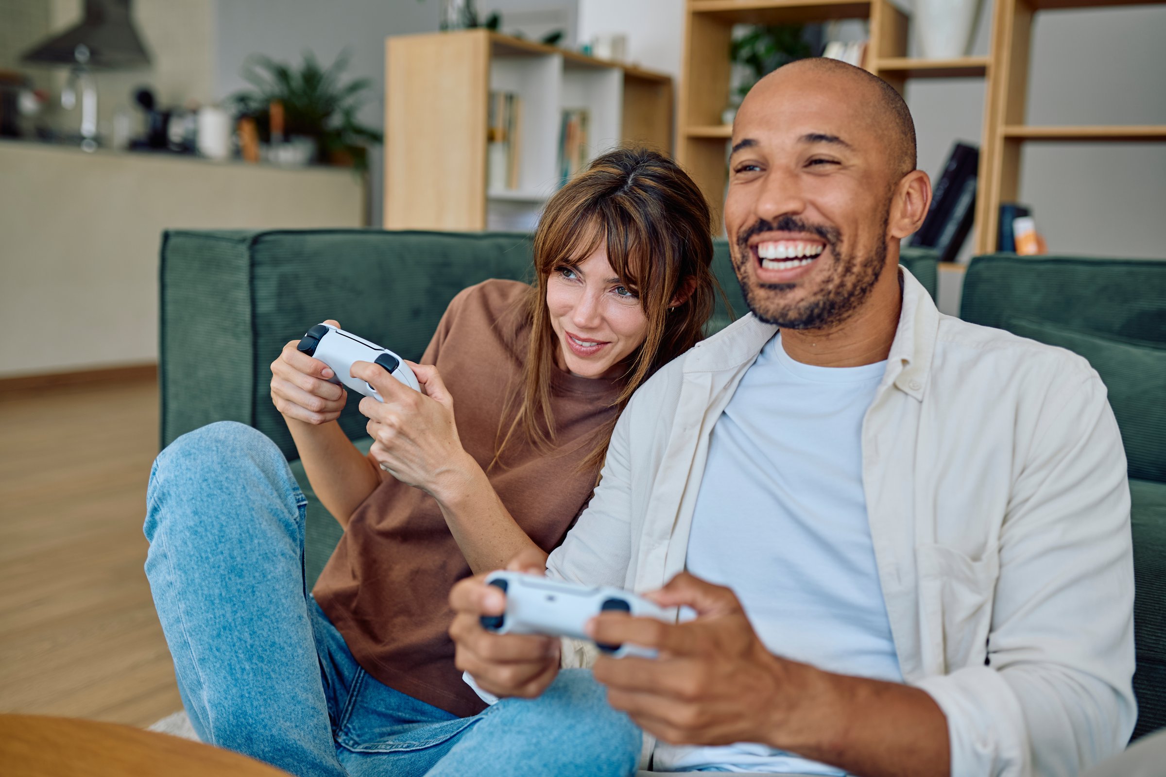 Cheerful couple enjoying quality time together, playing video games on the sofa in their cozy living room, sharing laughter and excitement