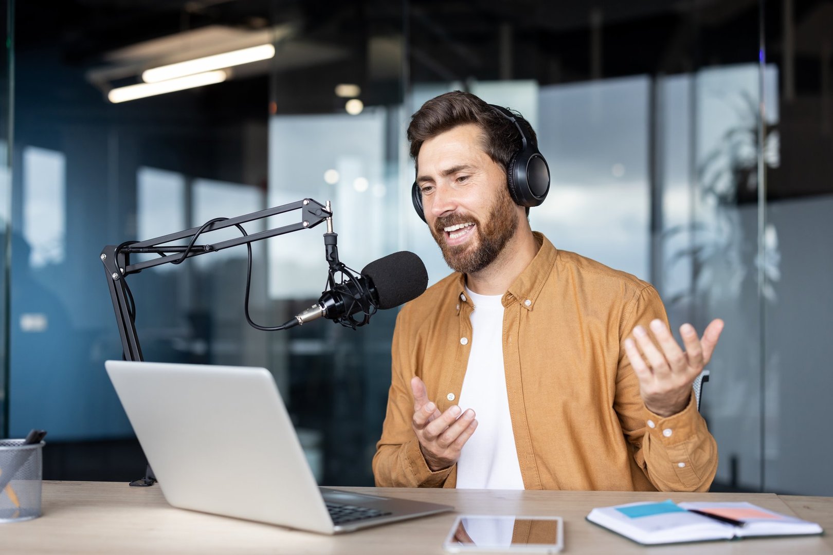 Podcaster in a professional setting recording content with a microphone and laptop in a modern office ambiance. He's efficiently combining technology with communication