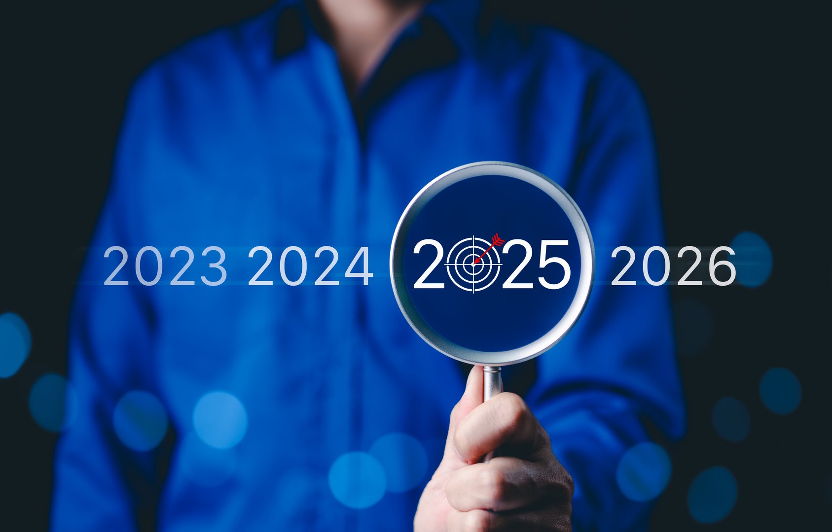 Focus on 2025 Business Goals and Future Planning. A person holding a magnifying glass highlighting 2025 with a target icon, future goals, strategy, and planning for the coming years. trends 2025,