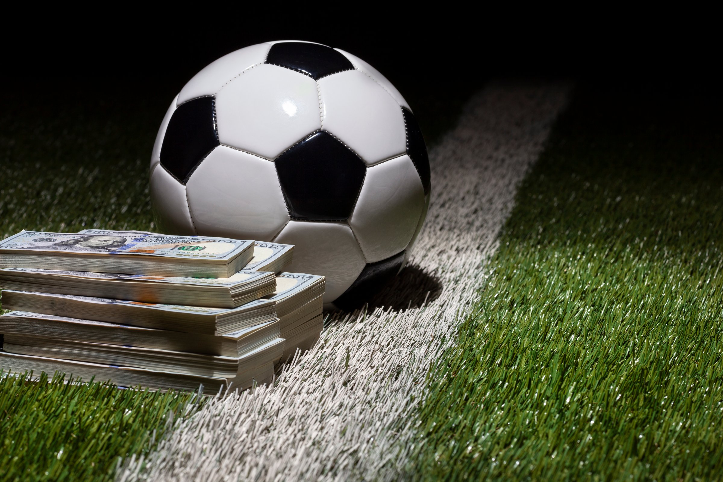 A soccer ball on grass field with stripe by stacks of one hundred dollar bills