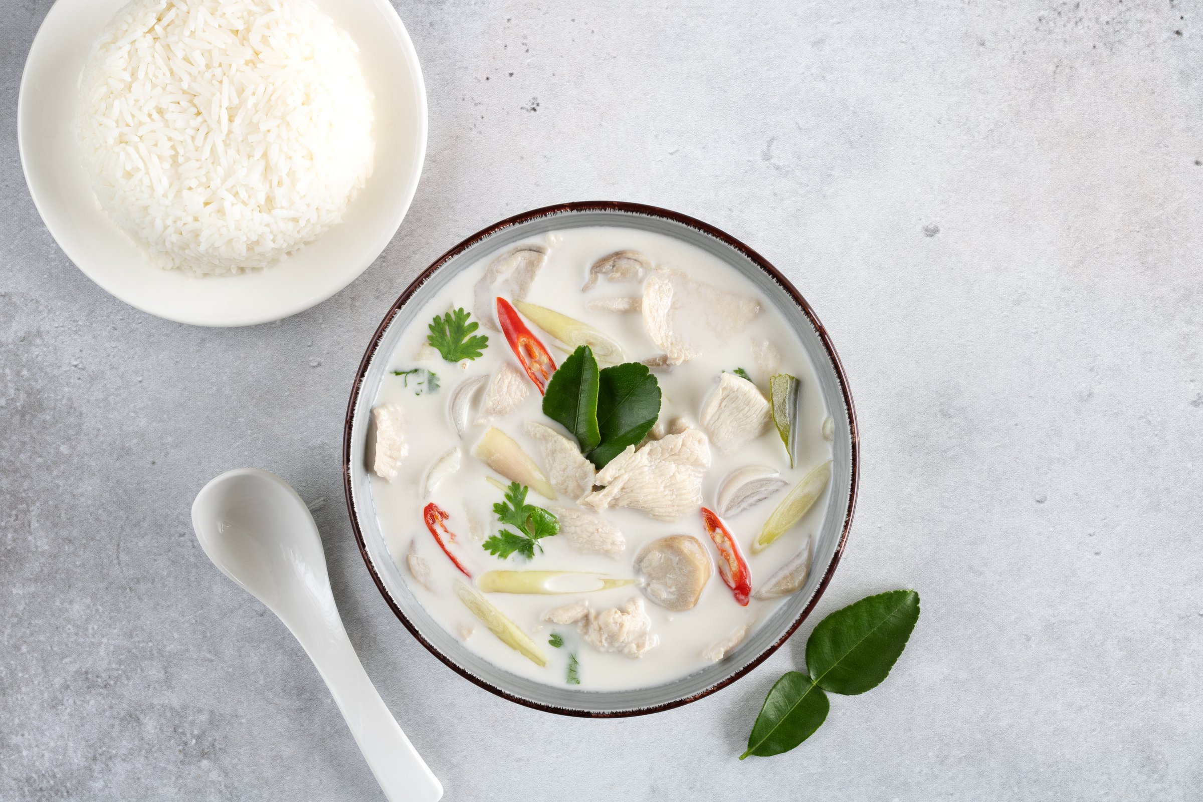 Soup Tom Kha Gai with chicken, lemongrass, kaffir, chili, lime and rice on a gray background, top view. Thai spicy soup with coconut milk. Thai traditional food.
