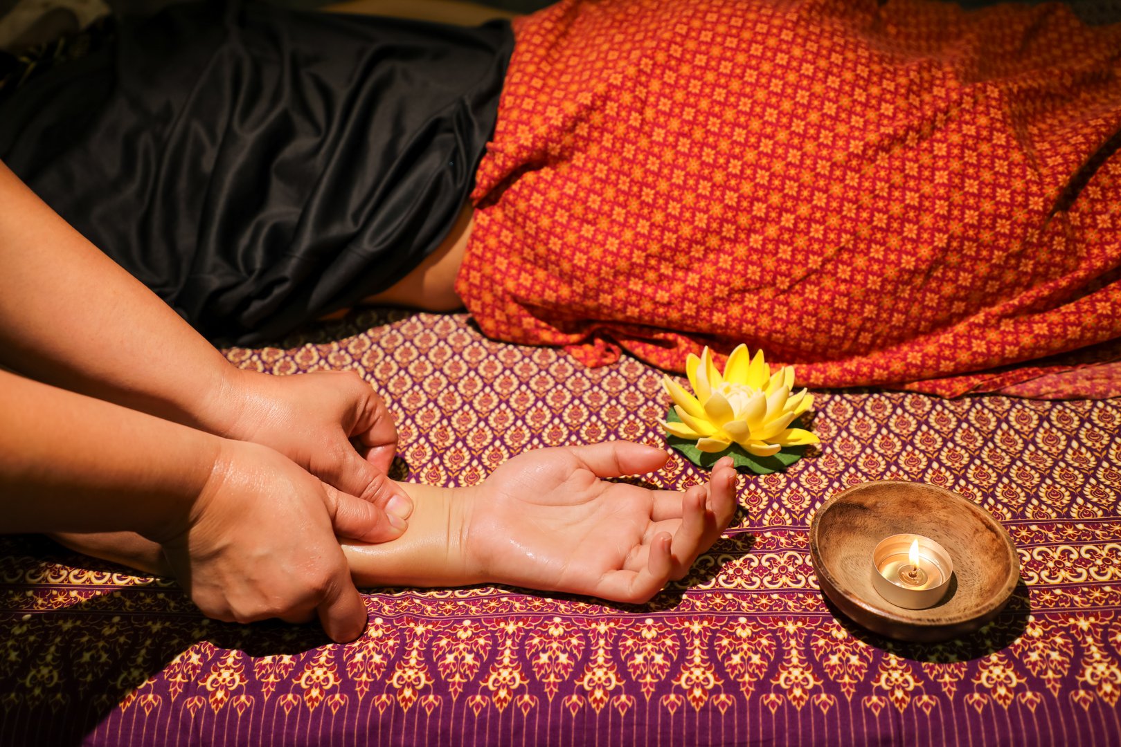 A girl gets a relaxing massage in a Thai massage parlor. A candle burns next to her and a yellow lotus flower lies.
