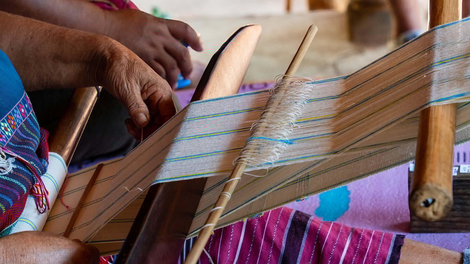 A close-up view of a traditional wooden weaving loom in use, with fine thread stretched across the frame and guided by hand. Captured in Mae Hong Son, northern Thailand, the image highlights a rural home workshop and the manual craft methods of local textile production. This scene reflects Southeast Asian artisan skills, generational techniques, and small-scale production in village contexts.