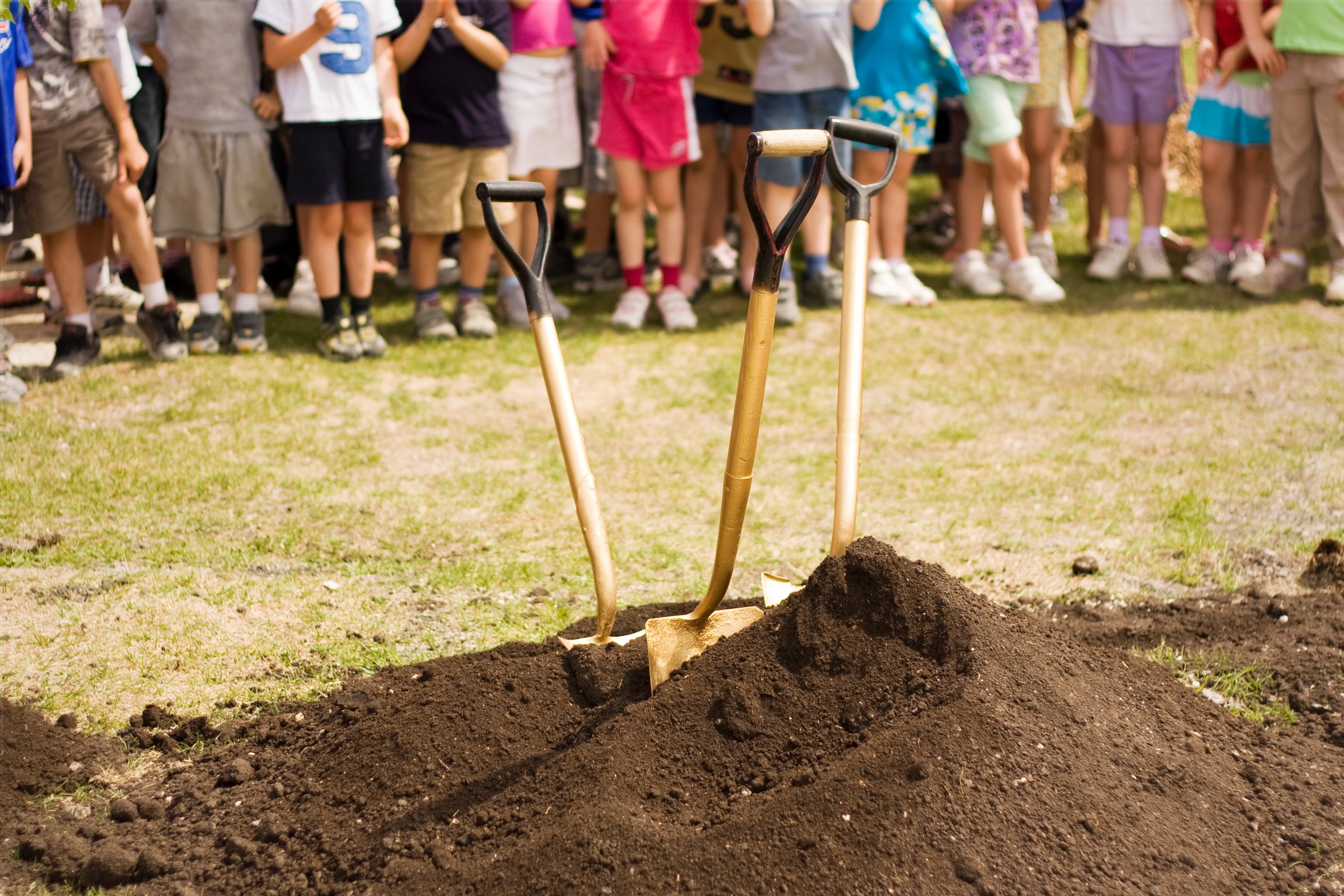 Young school children in background with three shovels in foreground.  Taken at the grand opening of a school's renovated park and green space.