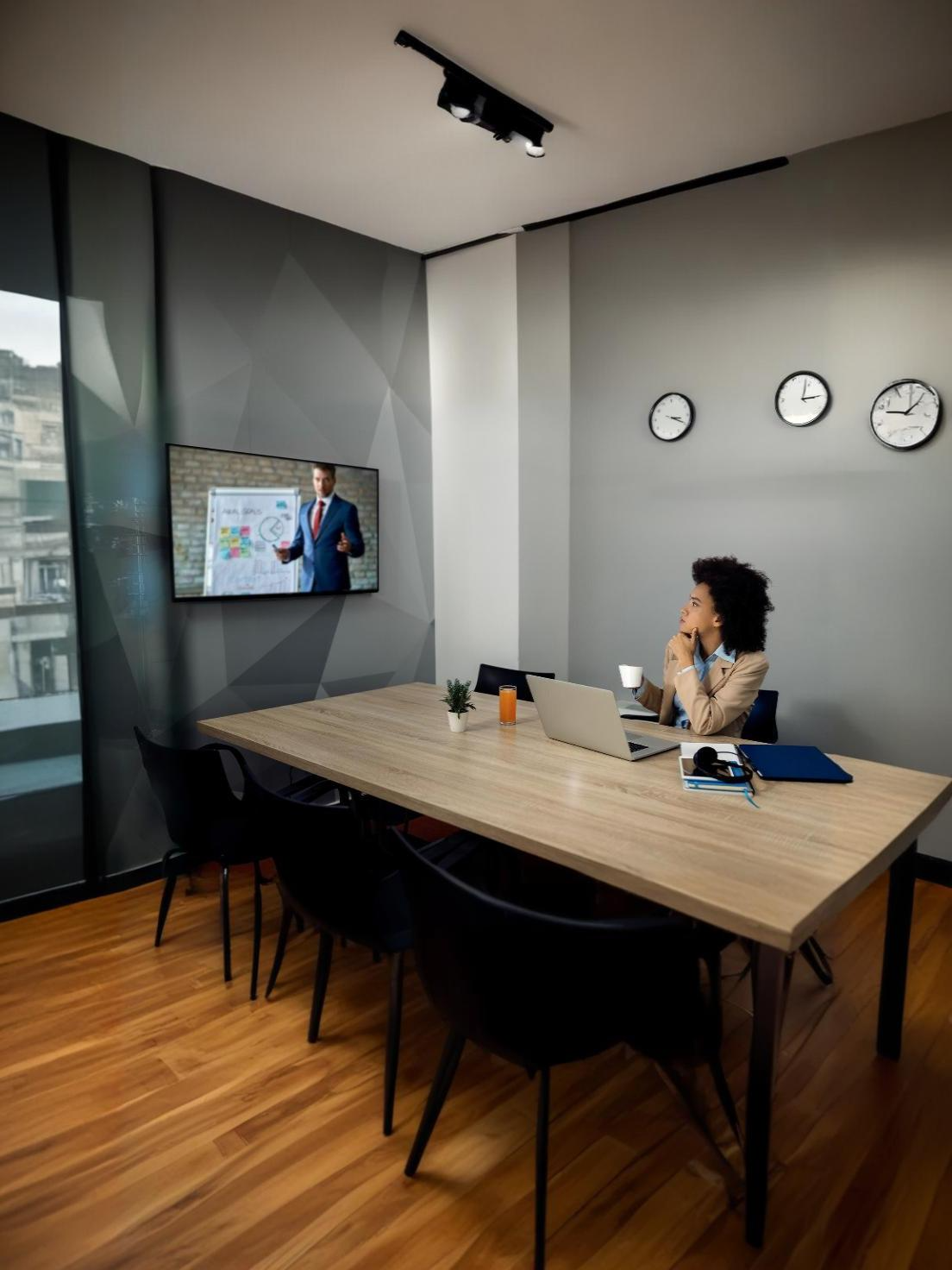 Person in a modern office watching a presentation on a wall-mounted screen, with clocks showing different time zones.