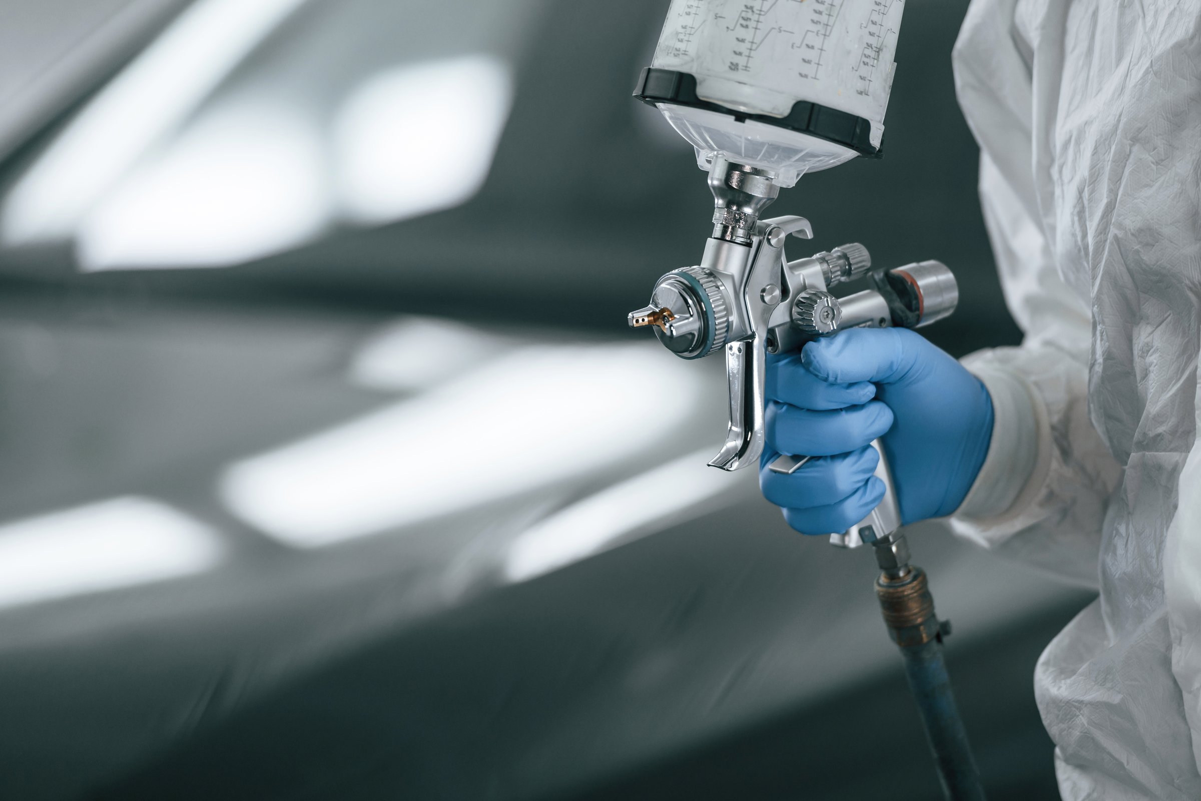 Focused close up view. Man is holding spray gun for painting a car.