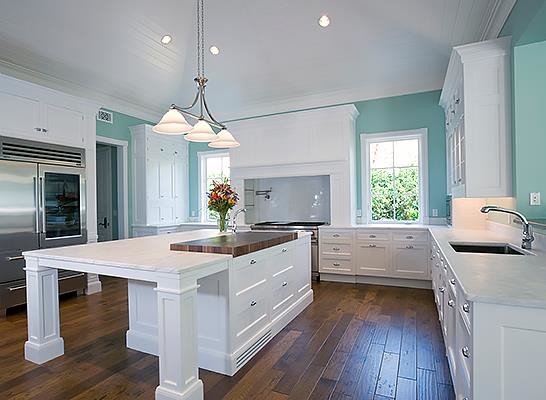 Modern kitchen with white cabinets, an island with marble countertop, hardwood floors, and teal walls.