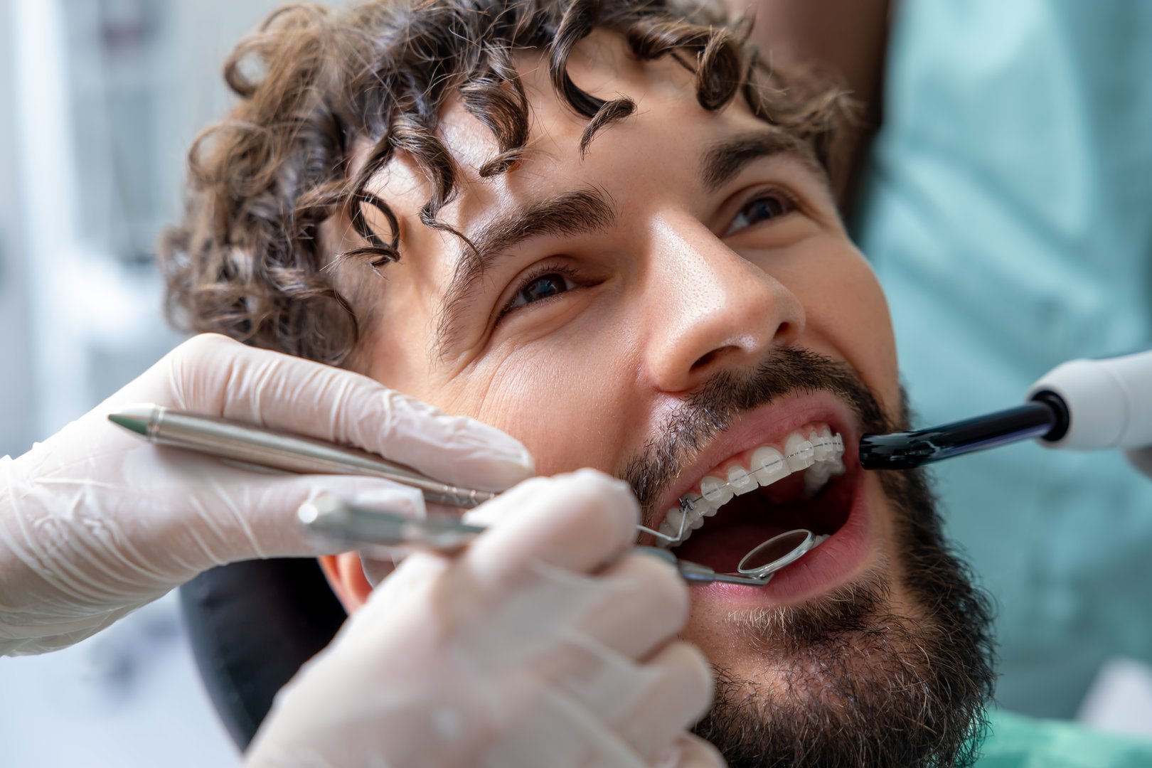 Bearded patient sitting in dental chair receiving oral examination or professional treatment from skilled dentist