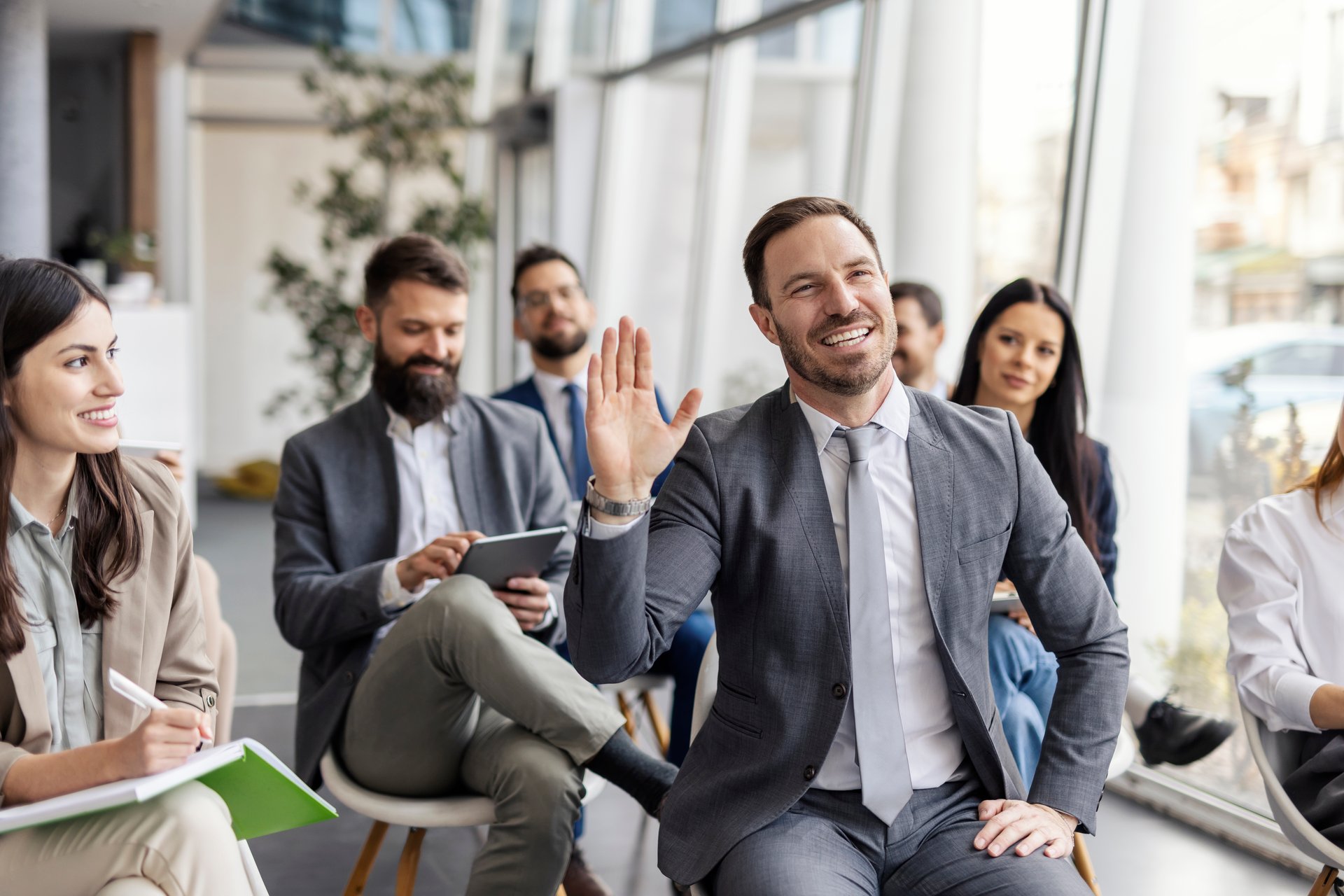 Corporate worker sitting in auditorium with his team members at boardroom and asking questions while having his hand raised.