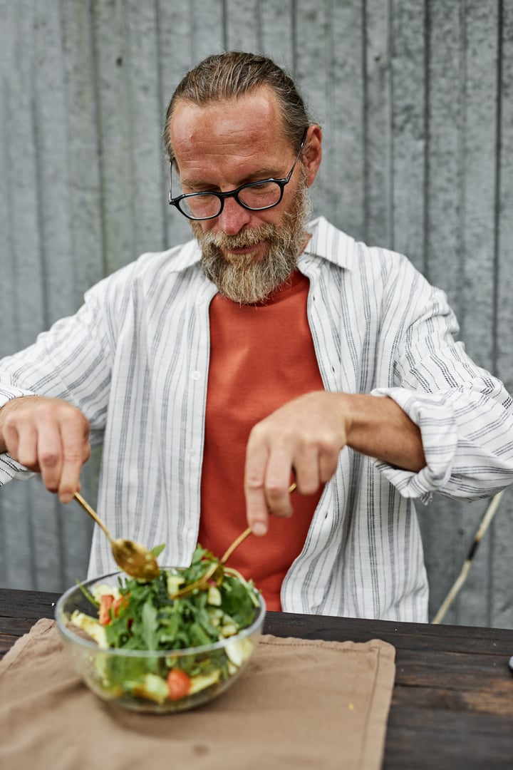 Vertical portrait of bearded mature man wearing casual outfit mixing salad while enjoying healthy lunch in outdoor cafe