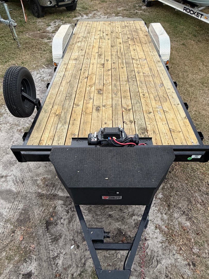 A flatbed trailer with dual axles, black frame, and wooden platform, designed for transporting vehicles or heavy loads.